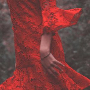 Een zwierige rode jurk. De vrouw die hem draagt doet zich voor als opgewekt en blij. Je ziet alleen de jurk, niet haar gezicht. Een vrolijke kleur tegen een donkere achtergrond.