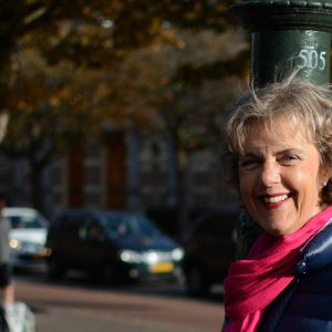 Een vrouw staat met haar gezicht half in de zon op een gracht in Den Haag. Zij straalt vertrouwen uit.