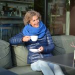 Een vrouw zit buiten op een terras in de late najaarszon en geniet van een kop koffie