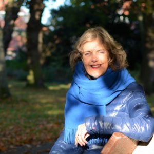Een vrouw zit op een bankje in het park. Het lage licht in de herfst tovert schaduwen op haar gezicht.