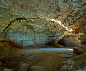 Een ondergrondse grot met prachtig gesteente, waarin door een spleet in de rotsen licht naar binnen valt.