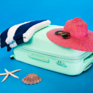 een mintgroene koffer, maar daarop een blauw wit gestreepte handdoek en een roze zonnehoed met zonnebril. Vakantietijd.