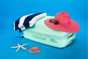 een mintgroene koffer, maar daarop een blauw wit gestreepte handdoek en een roze zonnehoed met zonnebril. Vakantietijd.